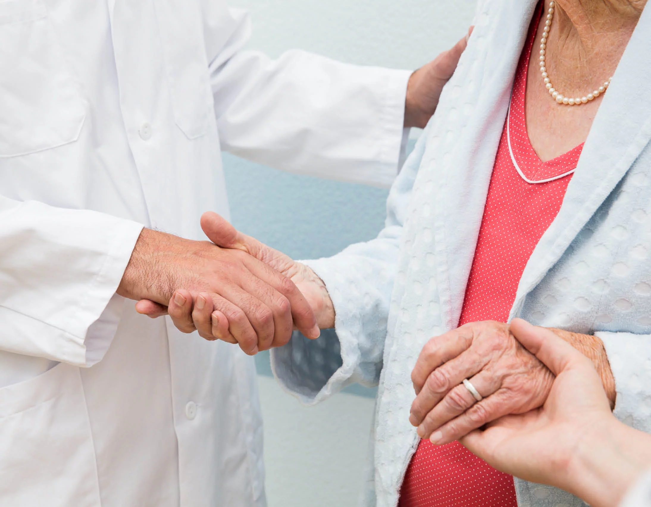 ältere Dame wird von Arzt und Pflegefachperson die Hände gereicht