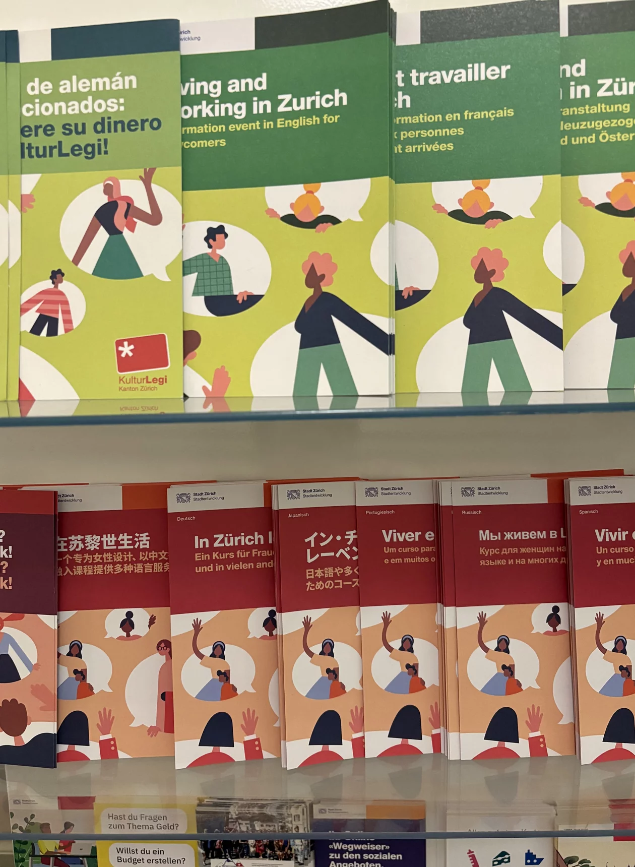 Auf einem Gestell sind Broschüren in vielen verschiedenen Sprachen aufgelegt. Auf dem Cover sind gemalte Männer und Frauen. 