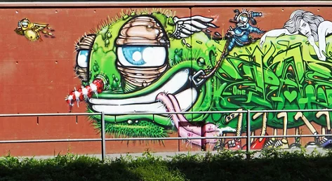 Ein farbiges Graffiti an einer Mauer entlang einem Spaziergängerweg.  