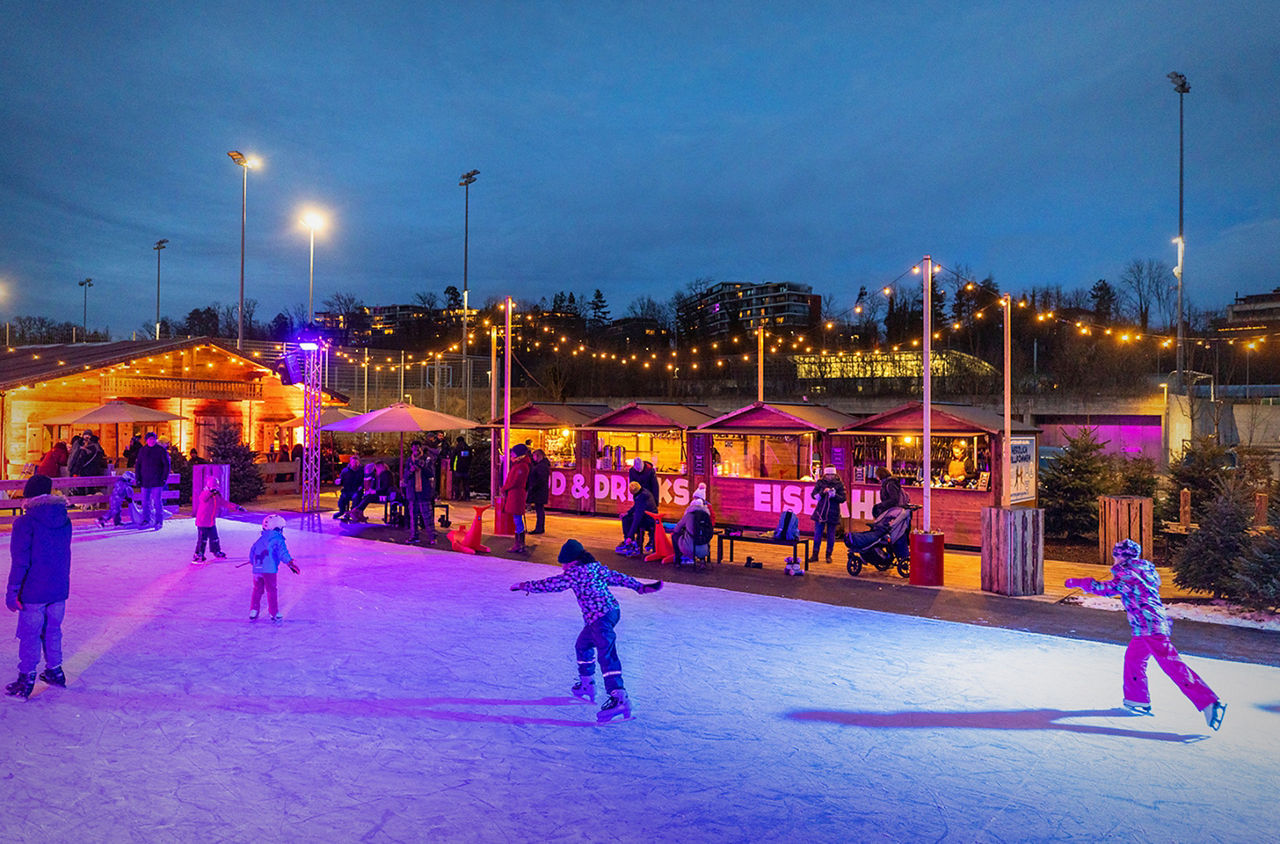 Schlittschuhlaufen am Winterzauber Adliswil mit Marktständen im Hintergrund.