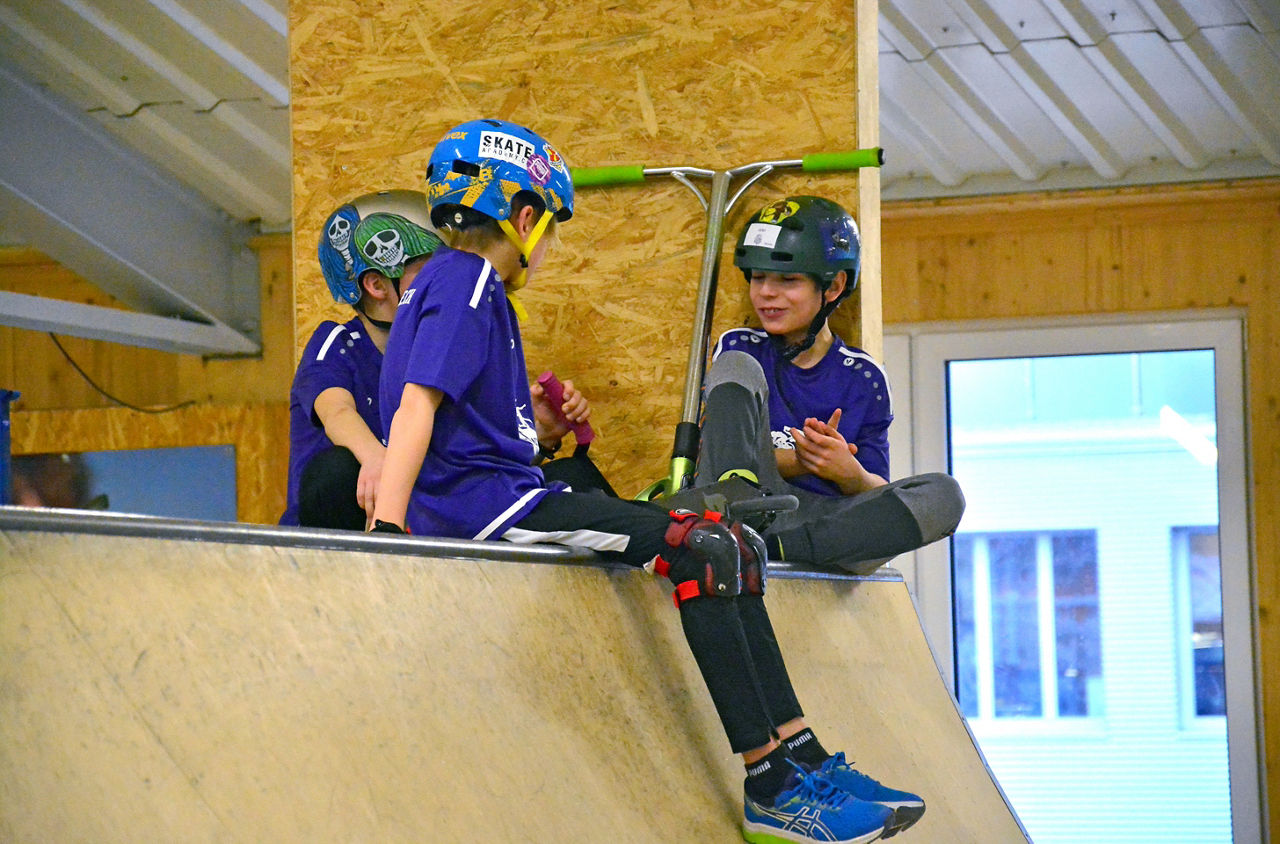 Drei Kinder sitzen mit ihren Scooters auf der Halfpipe im Geisterkickboarder GKB Skatepark in Wetzikon.