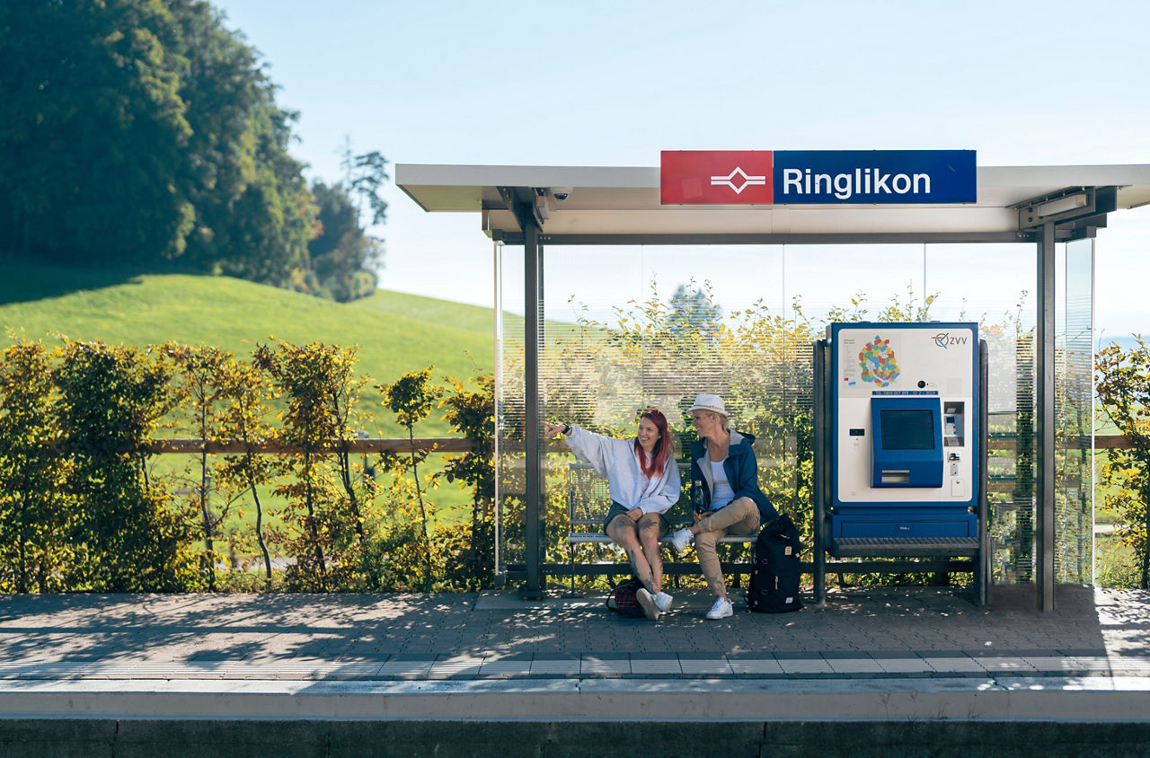 Zwei Frauen sitzen an der SZU-Haltestelle Ringlikon auf einem Ausflug