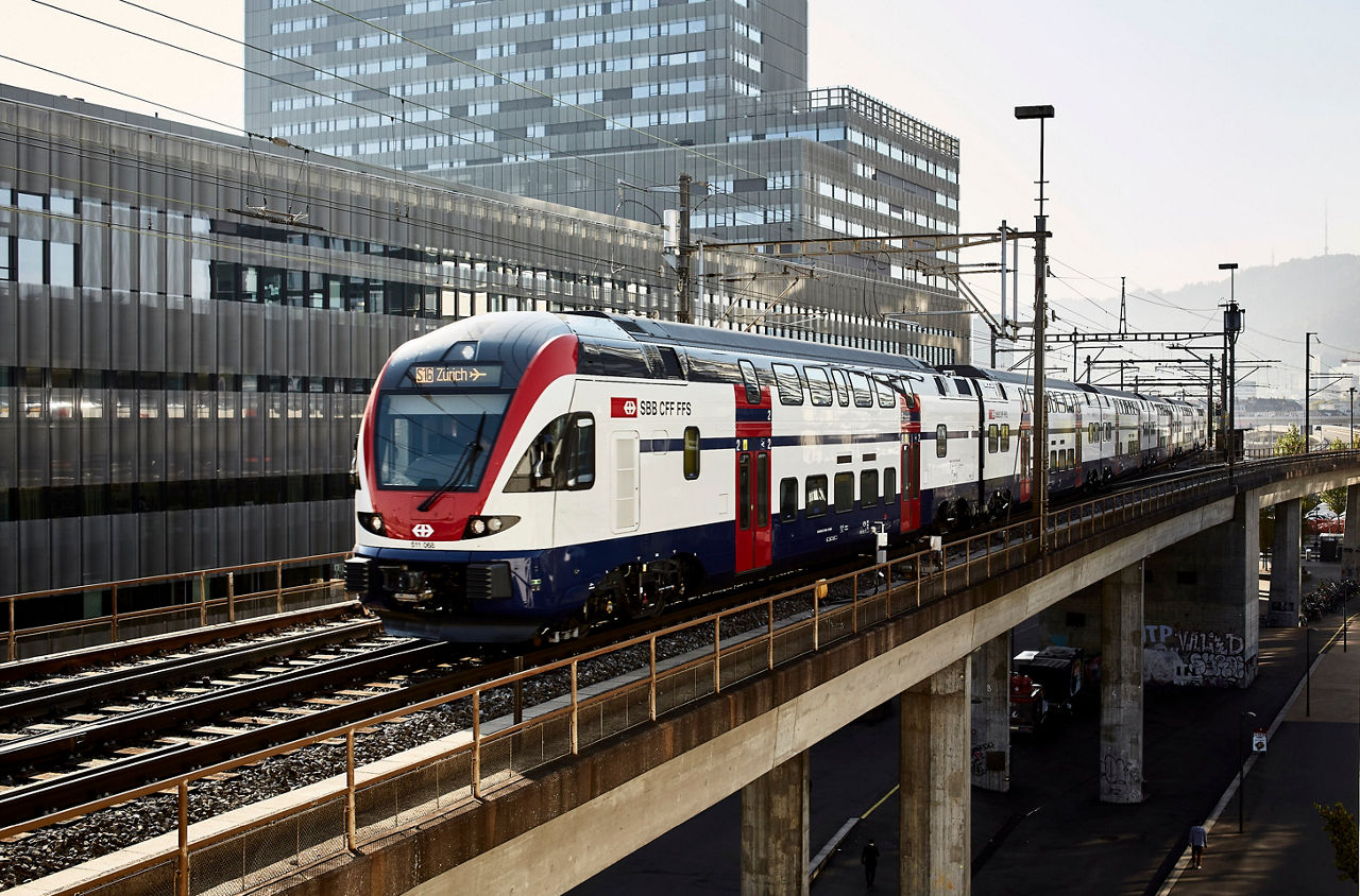 Bild vom Bahnhof Wiedikon mit Zug und Passagieren am Perron. 