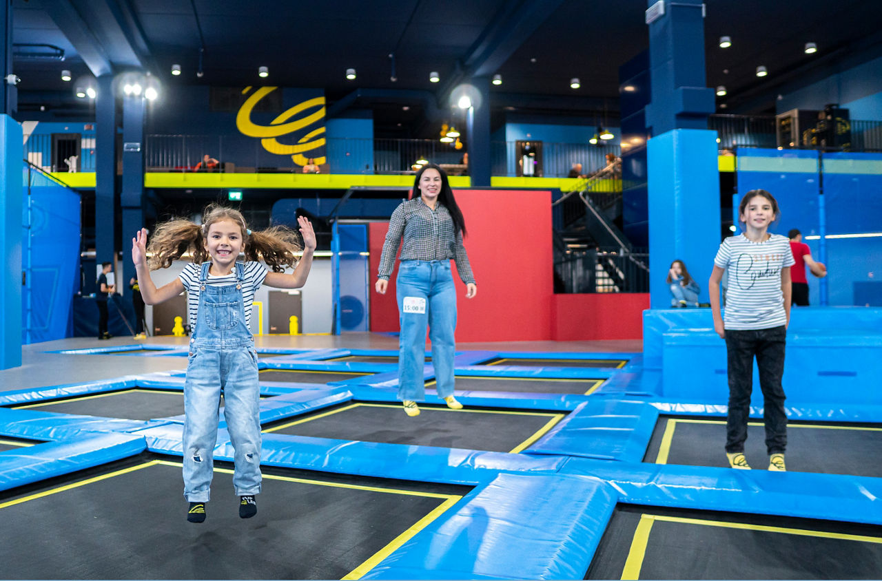 Eine erwachsene Person und zwei Kinder beim Springen auf Trampolinen im Flip Lab Rümlang. 