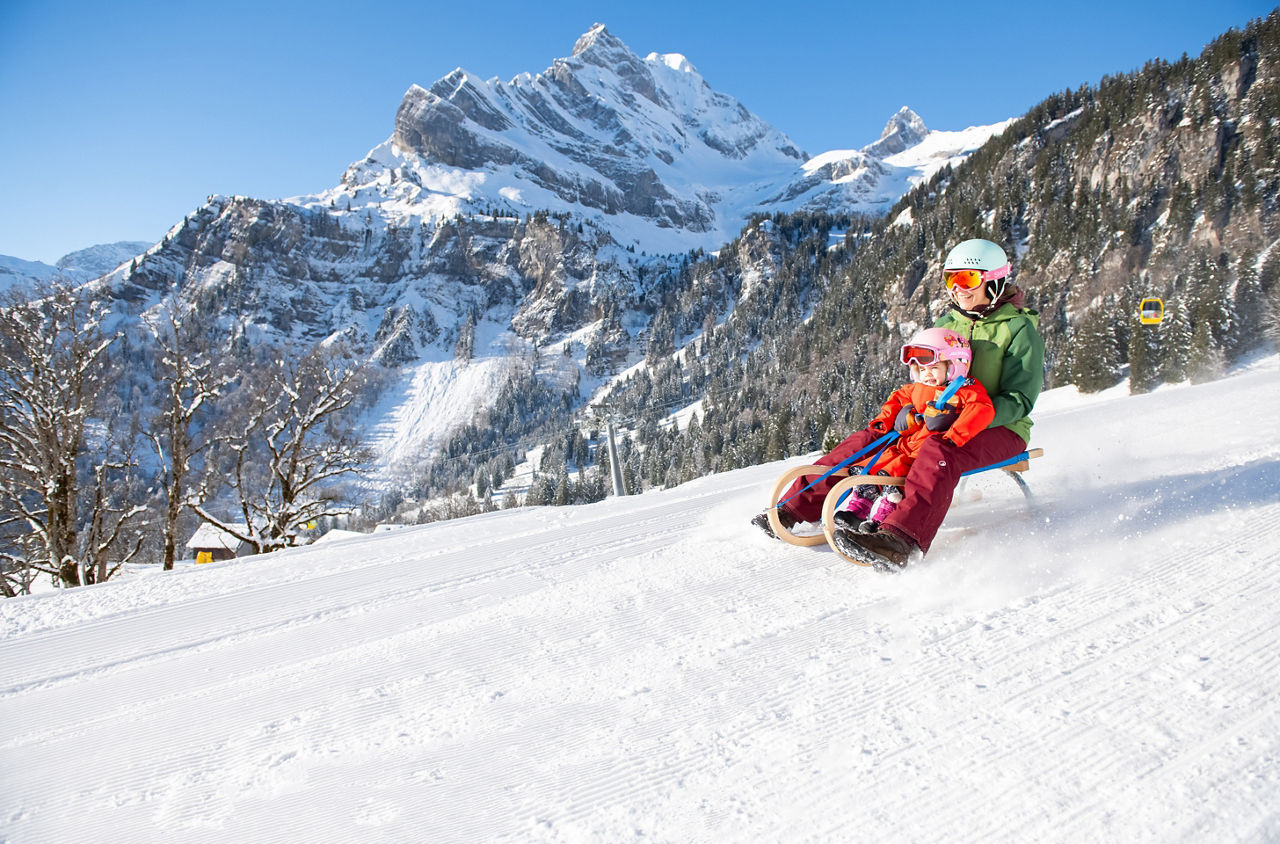 Eine erwachsene Person und ein Kind auf einem Schlitten in Braunwald. 